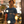 Load image into Gallery viewer, Chichiyasu Milk Coffee graphic tee inspired by the delicious Japanese coffee drink. Cute graphic tee with a coffee colored design on a navy short-sleeve t-shirt. Cute Japanese graphic tee with Japanese characters and an illustrated design of Chichiyasu Milk Coffee. A cute simple shirt for men or women. Modeled on an Asian man with a tattoo inside a cafe.