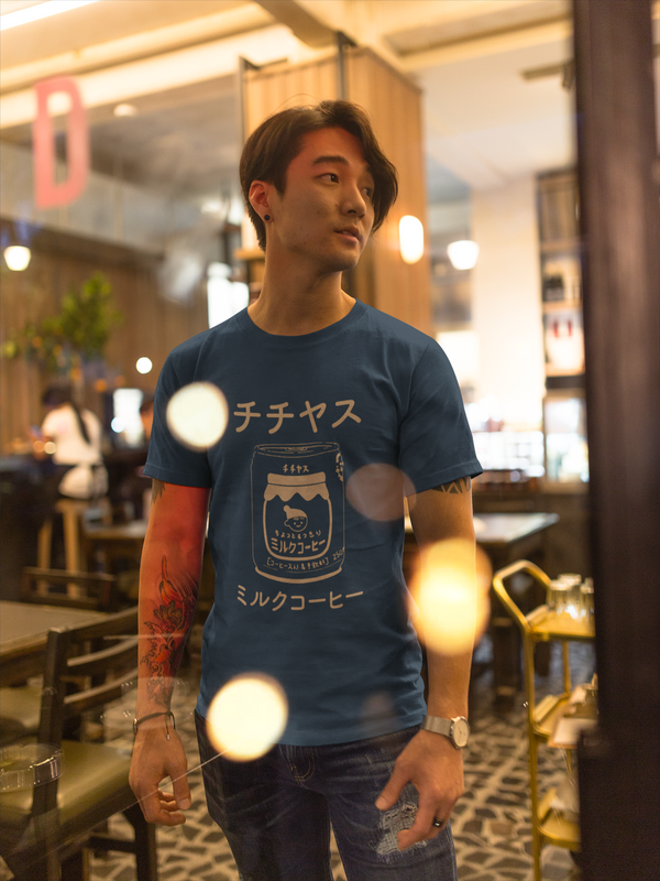Chichiyasu Milk Coffee graphic tee inspired by the delicious Japanese coffee drink. Cute graphic tee with a coffee colored design on a navy short-sleeve t-shirt. Cute Japanese graphic tee with Japanese characters and an illustrated design of Chichiyasu Milk Coffee. A cute simple shirt for men or women. Modeled on an Asian man with a tattoo inside a cafe.